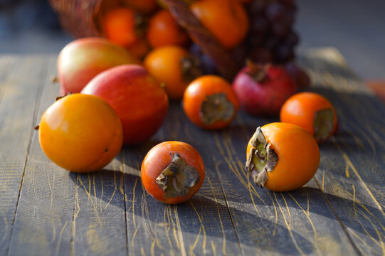 Selective focus on fresh orange persimmons on a wooden table with blurred fruit basket