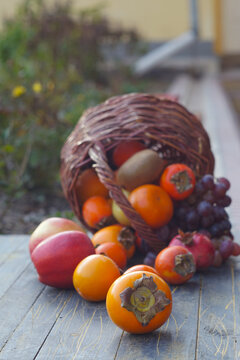 Vertical shot of autumn fruits spilling from a wicker basket on wooden surface.