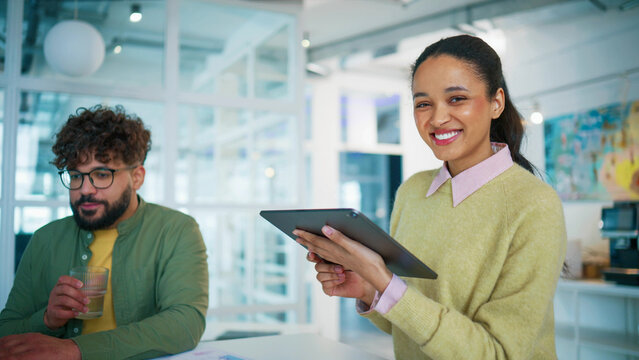 Office teamwork scene with two colleagues working. Female employee holding tablet and reviewing project data. Male coworker drinking water near laptop. Focusing on reports and online analytics.