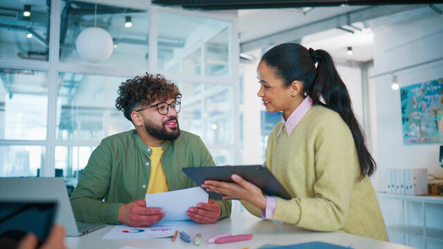 Bright office moment with colleagues working together. Smiling female employee holding tablet and checking results. Male coworker reviewing printed report. Discussing business progress and strategy.