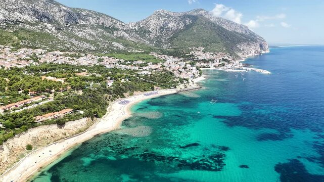 Aerial 4K footage of the crystal-clear turquoise sea off Cala Gonone, Sardinia, on a sunny summer day. Calm Mediterranean waters, blue sky, and pristine coastline create a stunning natural seascape
