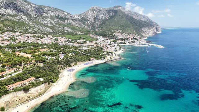 Aerial 4K footage of the crystal-clear turquoise sea off Cala Gonone, Sardinia, on a sunny summer day. Calm Mediterranean waters, blue sky, and pristine coastline create a stunning natural seascape