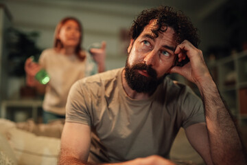 Man feeling frustrated and overwhelmed during couple argument at home, woman yelling in background