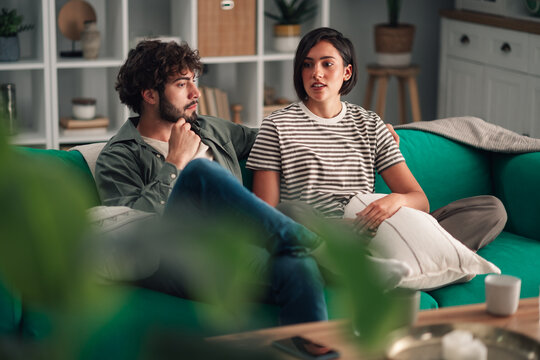 Young couple sitting on couch having serious conversation at home, discussing problems in their relationship