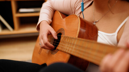 Fototapeta premium Woman playing acoustic guitar, strumming strings and enjoying leisure at home. Learning and practicing musical skills