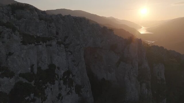Dramatic drone semi-circle left pan showcasing a natural stone gateway on a hill top, revealing a vibrant sunset horizon. High quality 4K video.