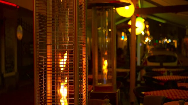Gas patio heater burning at night on an empty restaurant terrace. Outdoor gas heater providing warmth and ambiance on a chilly evening at a cafe terrace, with decorative lights