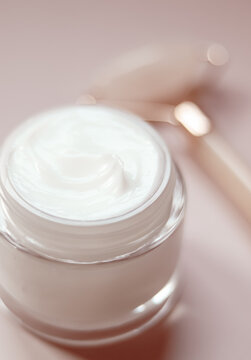 Face cream in a glass jar with rose quartz roller for daily skincare routine and luxurious beauty treatment