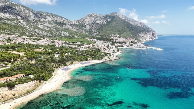 Aerial 4K footage of the crystal-clear turquoise sea off Cala Gonone, Sardinia, on a sunny summer day. Calm Mediterranean waters, blue sky, and pristine coastline create a stunning natural seascape