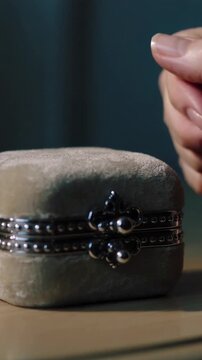 Vertical video: Lifting hand closing velvet box on table, latching clasp over white padding safely