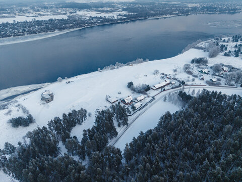 Aerial view of Doles sala on the Daugava river featuring snow-covered forests and houses in the winter landscape of Salaspils pagasts, Salaspils novads, Latvia.