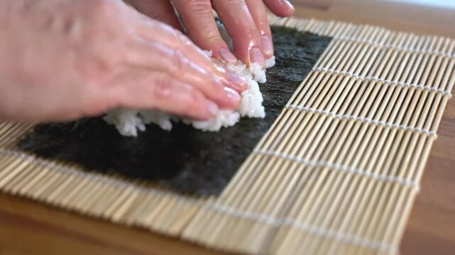 Chef spreading white rice on nori seaweed sheet for sushi.
