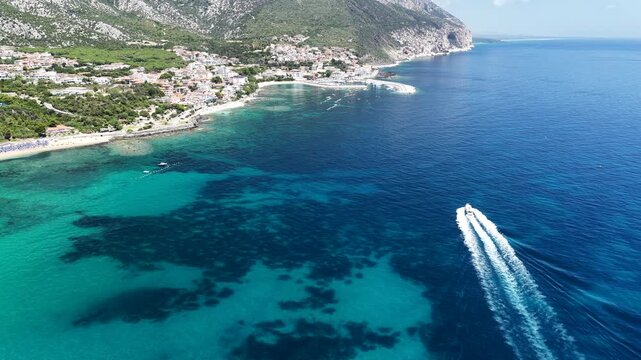 Aerial 4K footage of the crystal-clear turquoise sea off Cala Gonone, Sardinia, on a sunny summer day. Calm Mediterranean waters, blue sky, and pristine coastline create a stunning natural seascape