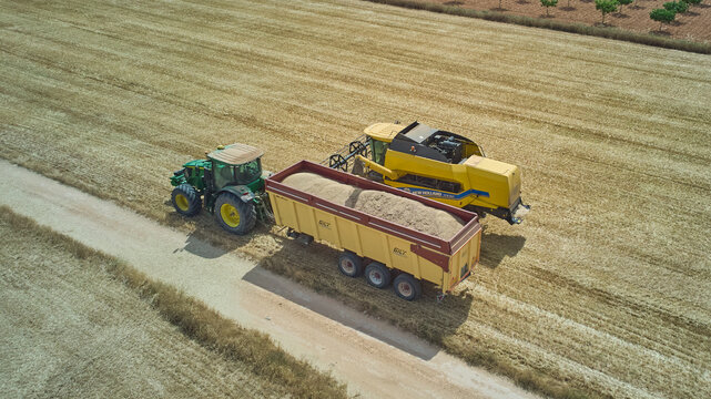 Aerial view of combine unloading harvested wheat grain into tractor trailer in field. Castilla-La Mancha, Spain - June 7, 2026.
