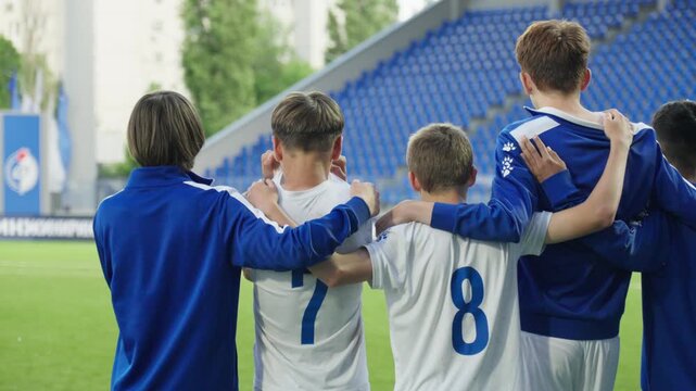 Football team players stand and hug while waiting for a penalty kick to be taken against them, view from behind