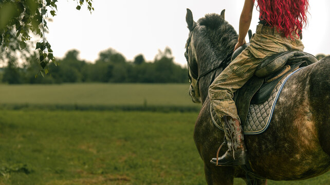 Woman with vibrant red hair rides a horse through a grassy field
