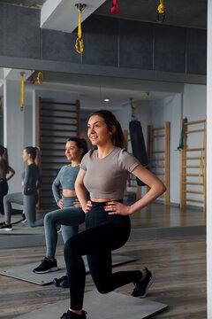 Woman doing a workout with lunges in a gym during daytime with another woman in the background