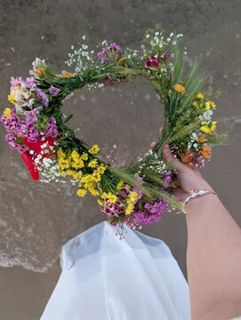 Hand holding a colorful wildflower wreath above sandy beach background. Traditional floral wreath associated with midsummer celebrations such as Kupala Night, Midsummer  and other seasonal folk 