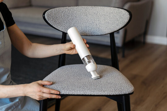 A woman cleans a chair with a cordless vacuum cleaner in her living room