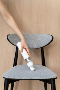 Woman cleans chair using small cordless vacuum cleaner in modern home