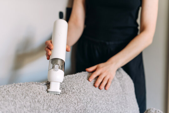 Woman uses cordless vacuum cleaner to clean couch in modern living room
