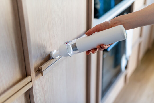 Woman uses cordless vacuum cleaner in modern kitchen for quick clean up