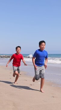 Two brothers playing tag on the beach in Santa Monica. Slow Motion. Vertical video.