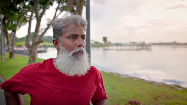 Mature Indian man with a beard jogging in a lakeside park In Singapore. Slow motion.