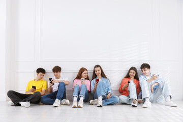 Fototapeta premium Group of teenagers with different smartphones near white wall indoors, space for text