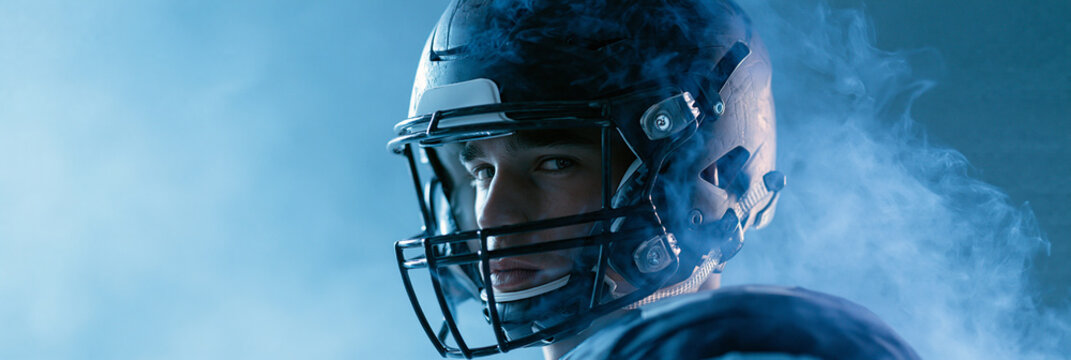 Male athlete in a football helmet surrounded by dramatic smoke and blue lighting.