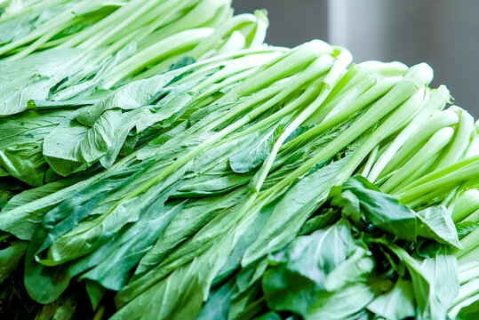 Fresh green choy sum vegetables arranged in a pile, healthy leafy greens for cooking, organic produce from a local market, vibrant vegetable background