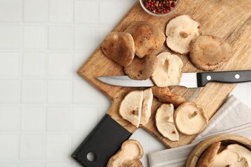 Fototapeta premium Raw shiitake mushrooms and knife on white tiled table, flat lay. Space for text