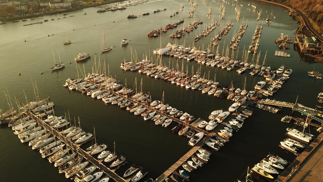 Aerial view of the marina with numerous sailboats and motorboats docked in rows, golden hour lighting, calm water, and coastal landscape in Kingswear, England, United Kingdom.