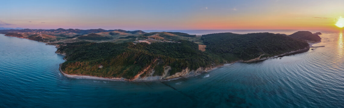 Ultra-wide aerial panorama showing the forested headland, remote beaches and open sea at Kepi i Rodonit in warm evening light.
