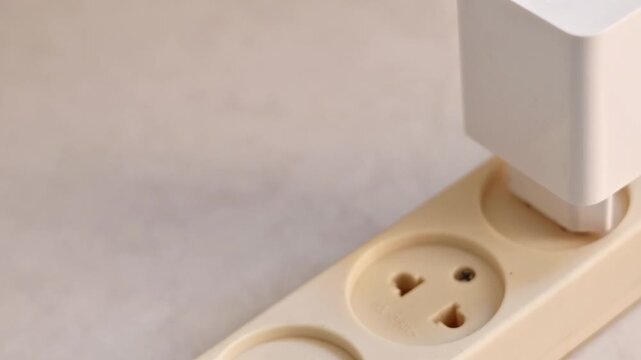 Close up of hand plugging a white smartphone charger adapter into an extension cord socket, mobile phone battery charging concept.