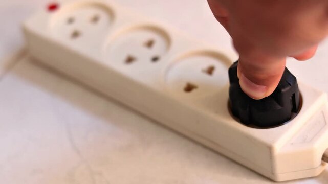 Close up of hand plugging a black power adapter into a white extension cord outlet, electricity and charging laptop concept.