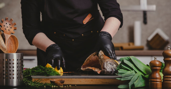 Private chef hands opening raw stuffed trout carcass on wooden board. Gourmet culinary preparation and premium catering service concept.