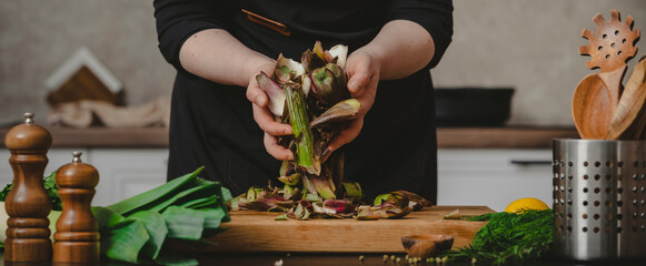 Obraz premium Private chef hands gathering organic artichoke waste pieces above table. Homemade cuisine preparation and traditional domestic lifestyle concept.