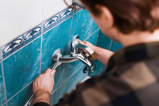 A handyman performs a faucet replacement using a wrench for plumbing DIY repairs. He is replacing an old faucet during a bathroom home renovation.