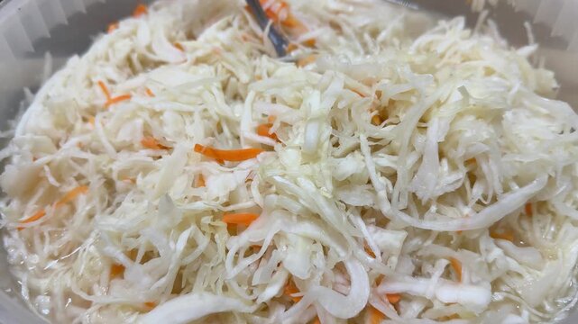 Fresh sauerkraut with carrot shreds displayed in transparent plastic container on market counter, market vendor presenting
