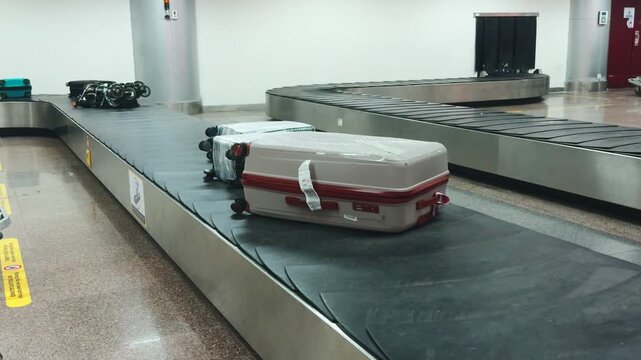 Airport baggage carousel conveying various pieces of luggage, including a grey and red suitcase, through the claim area, illustrating the common process of retrieving belongings after air travel