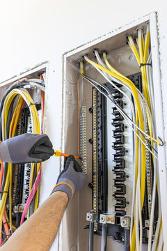 Close up view of professional electrician hands in work gloves tightening screw on ground bar with insulated screwdriver inside open electrical panel