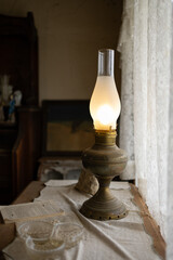 Vintage kerosene lamp glowing on a rustic table inside a cozy traditional room, retro oil lantern with warm light near a window © Iryna