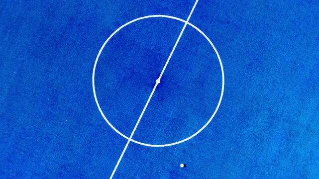 Aerial photograph of a blue artificial turf futsal field, with a white line down the center.