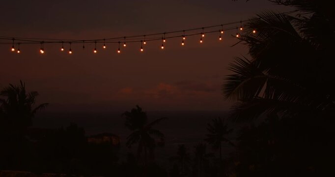 Warm string lights hanging over silhouette palm trees at dusk in Nusa Penida Indonesia