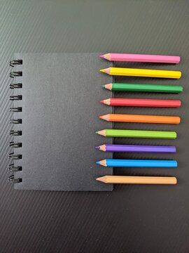Defocused view of black book with colourful pencils at the side isolated on black background 