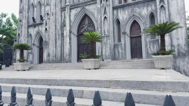 St. Joseph's cathedral in hanoi, vietnam, displaying its weathered gothic revival facade, classic architectural details, and stone steps leading to ancient entrances framed by potted plants