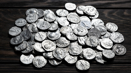 Pile of ancient Roman silver coins on a dark old wooden table. Close-up of antique metallic currency hoard. Historical money background, treasure concept © scaliger