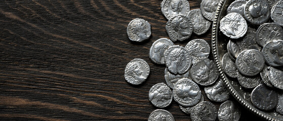 Ancient Roman silver coins on a dark wood background. Collection of antique denarii spilling from a vintage silver bowl. History concept. Copy space for text © scaliger