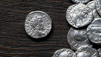 Close up of ancient Roman silver coins on a dark rustic wooden table. Macro view of a denarius with an emperor Septimius Severus. Money, antique and history concept. © scaliger